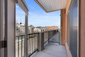 A balcony with a black railing and a view of buildings and cars.